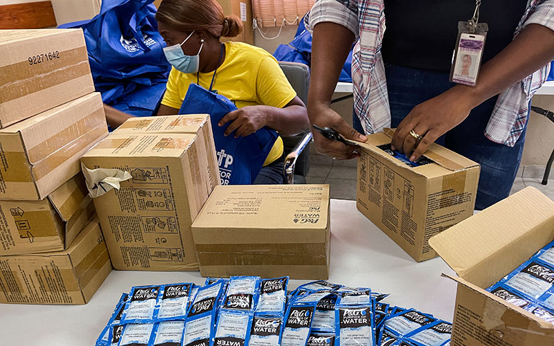 A woman wearing a yellow shirt stands next to a man in a blue shirt surrounded with boxes.