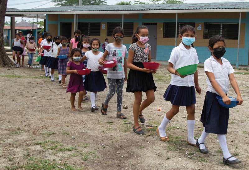 Young children standing in a line outside of school with food bowls