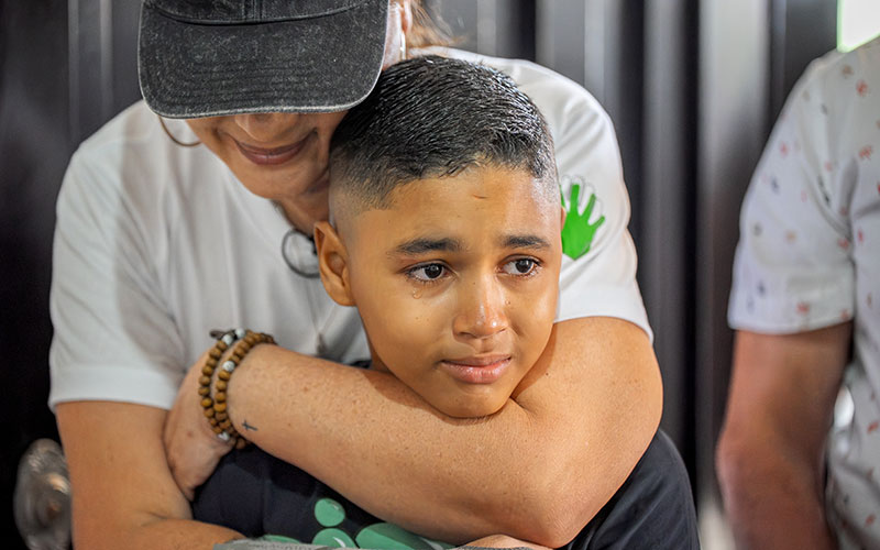 A woman embraces a young boy wearing a white shirt.