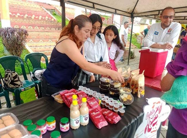 Several individuals gather around a table laden with food for young entrepreneurs in Colombia